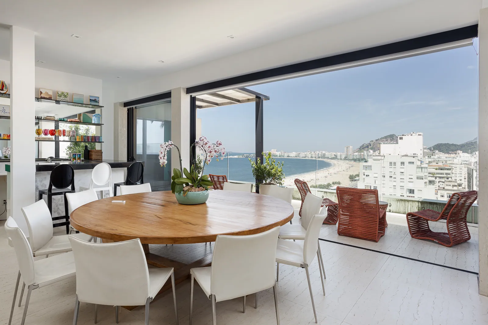 Dining table beside the glass, terrace and beach beyond
